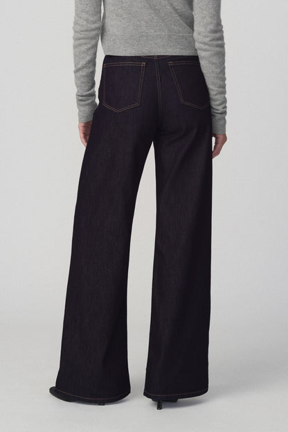 Back view of a woman modeling a light gray cropped cardigan and the mia petite dark wide-leg jeans in 'absolutely' color against a plain light gray studio background.