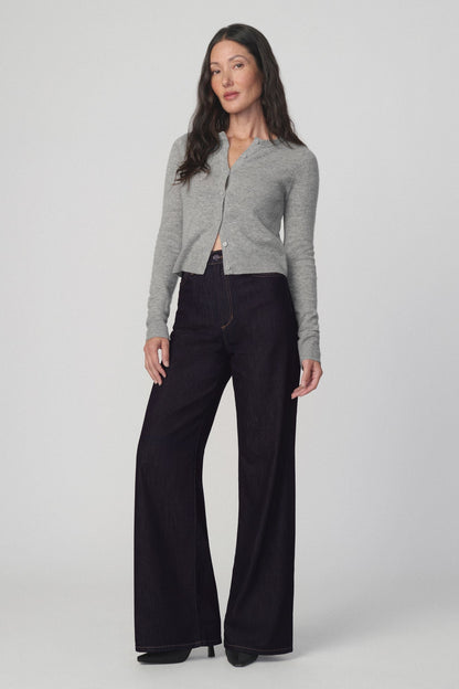 A woman modeling a light gray cropped cardigan and the mia petite dark wide-leg jeans in 'absolutely' color against a plain light gray studio background.
