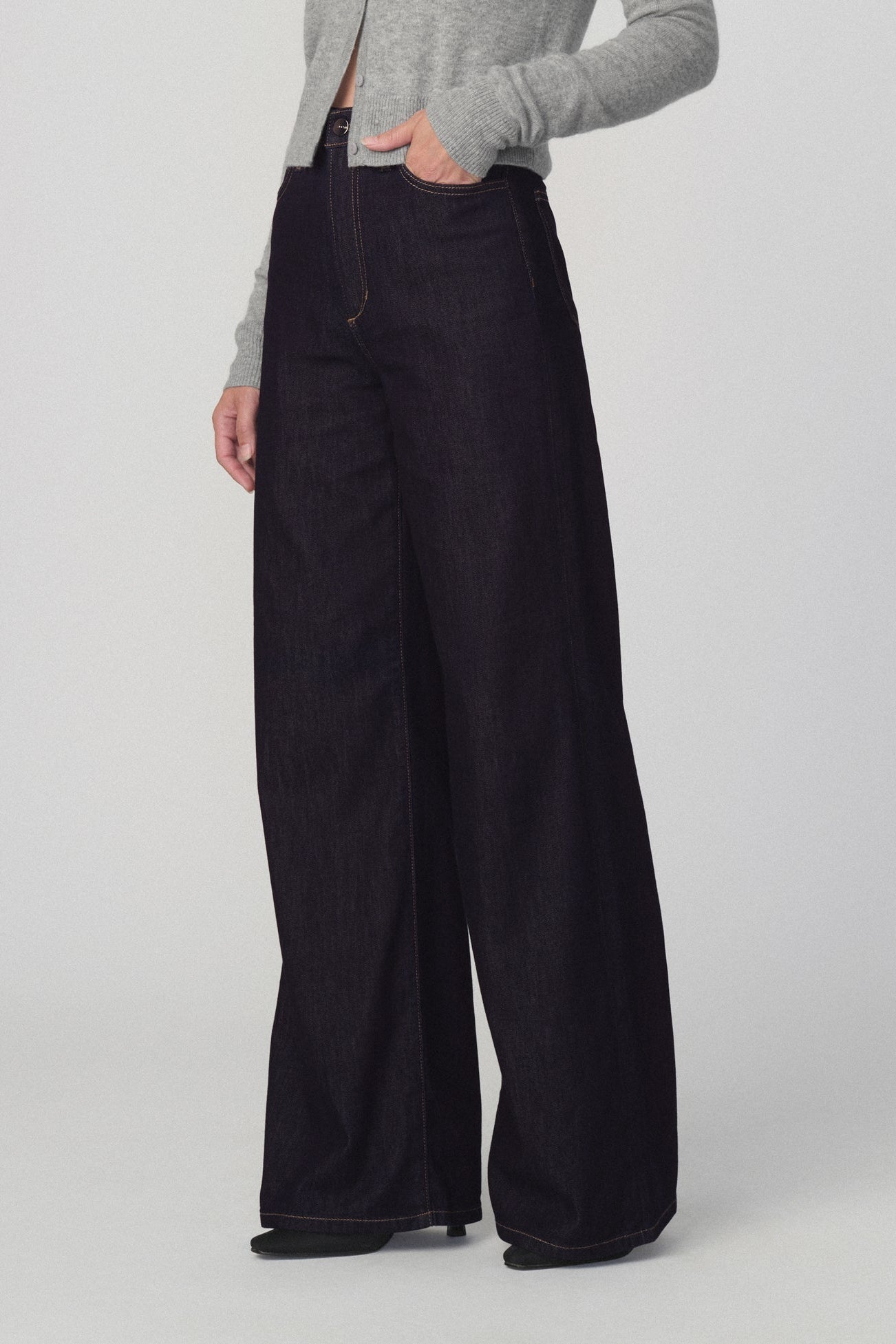Side view of a woman modeling a light gray cropped cardigan and the mia petite dark wide-leg jeans in 'absolutely' color against a plain light gray studio background.