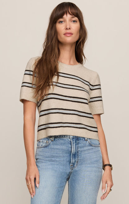 Front view of woman wearing a light oatmeal heather  striped Gatewood sweater and blue jeans on a plain background