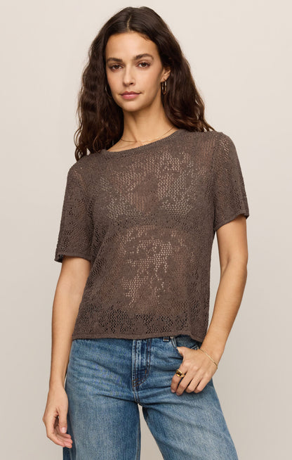 Woman wearing a cocoa latte knit top and blue jeans on a beige background