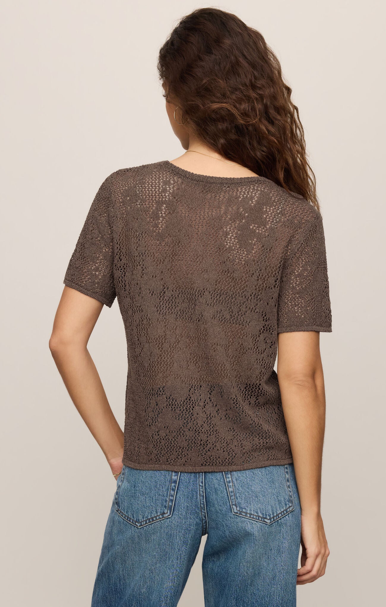 Back view of woman wearing a cocoa latte textured top and blue jeans on a beige background