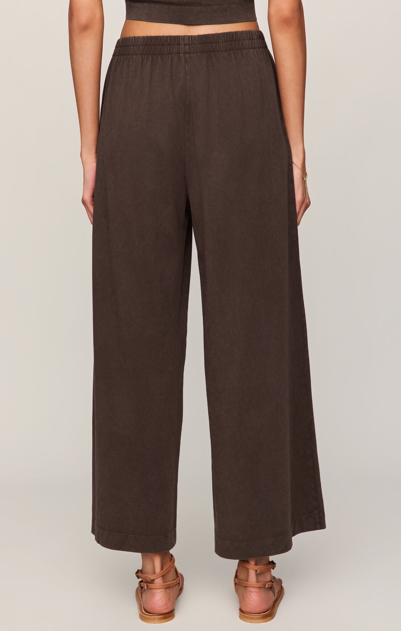 Back view of woman wearing dark chocolate "Scout" crop flare pants on a plain background