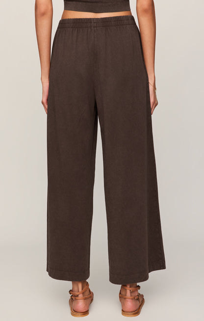 Back view of woman wearing dark chocolate "Scout" crop flare pants on a plain background