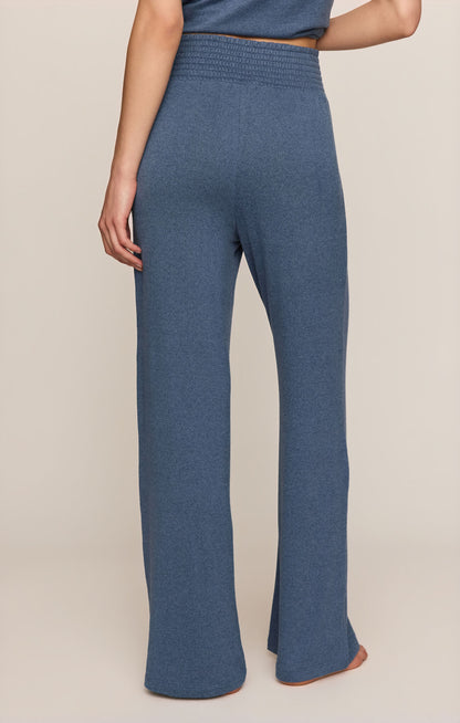 Back view of true navy smocked pants worn by a person on a beige background