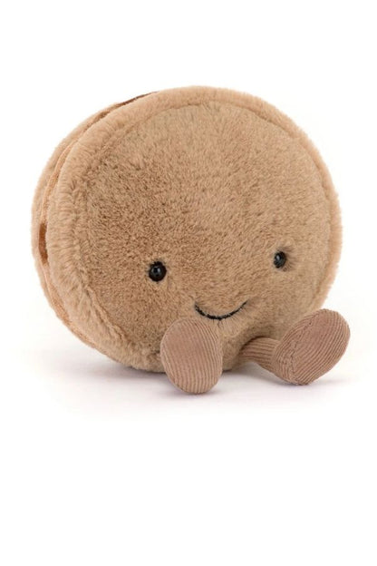 A round, soft plush toy shaped like a smiling macaron called "Mona Macaron" in a warm chocolate color, with small black eyes and a stitched smile, photographed on a clean white background.