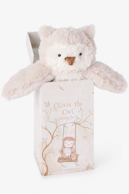 A plush owl named Olivia the Owl made of soft cream-colored plush fabric, emerging from its illustrated gift box. The box features a whimsical illustration of the owl on a swing and the text 'Olivia the OWL SNUGGLER' and 'ELEGANT BABY'.