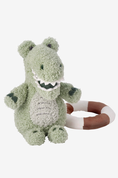 A plush dinosaur toy in light sage green with a textured, fuzzy fabric, featuring a brown and white ring puller attached to its back, set against a plain light gray background.