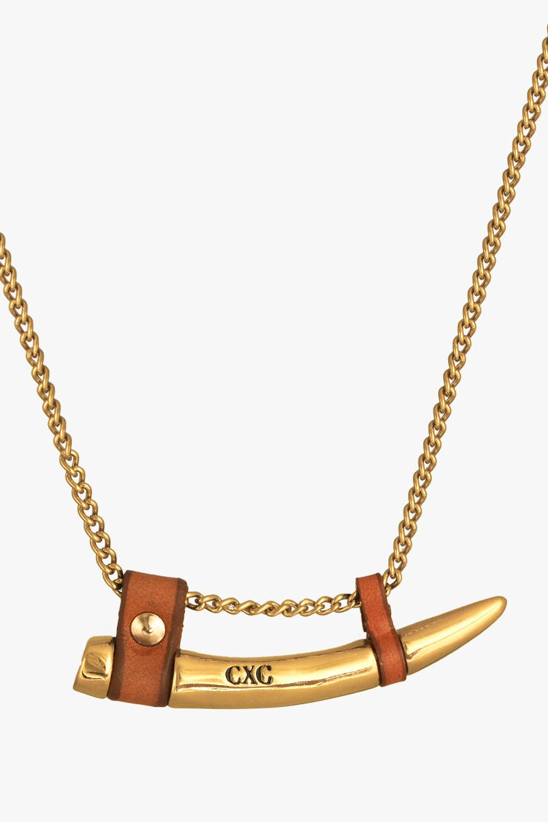 A gold-tone chain necklace featuring a curved fang shaped pendant with brown leather wraps and the engraved letters 'CXC'.