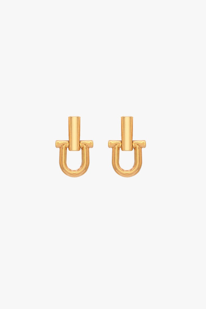 A pair of gold-toned U-shaped mini shackle stud earrings with a vertical post and small side tabs, shown on a plain light gray background.