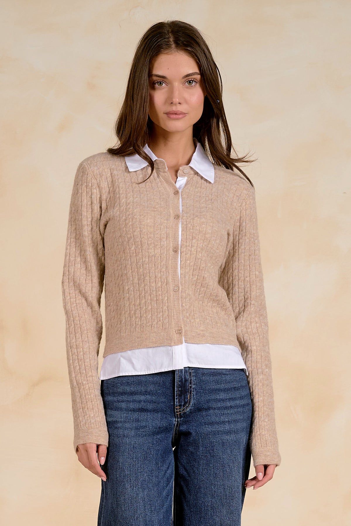 Woman wearing a beige cardigan with a white collar and bottom with blue jeans on a beige background