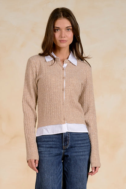 Woman wearing a beige cardigan with a white collar and bottom with blue jeans on a beige background