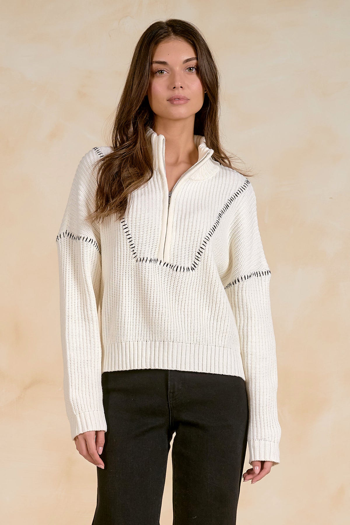 Woman wearing an off white ribbed quarter zip sweater with a zipper on a beige background