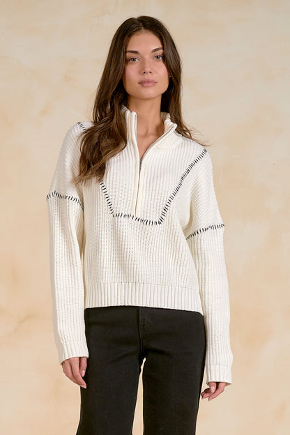 Woman wearing an off white ribbed quarter zip sweater with a zipper on a beige background