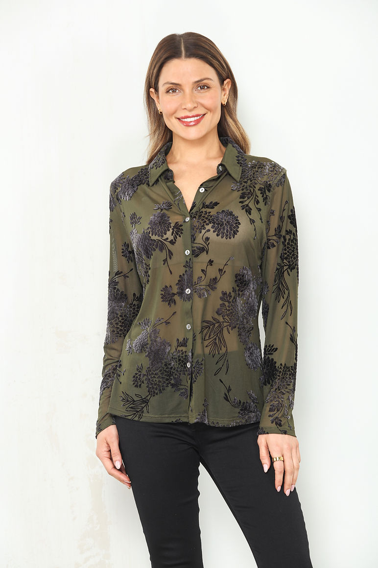 A woman modeling a long-sleeve button-up shirt with an olive green and black floral flocked sheer mesh pattern, paired with black pants, against a plain white background.