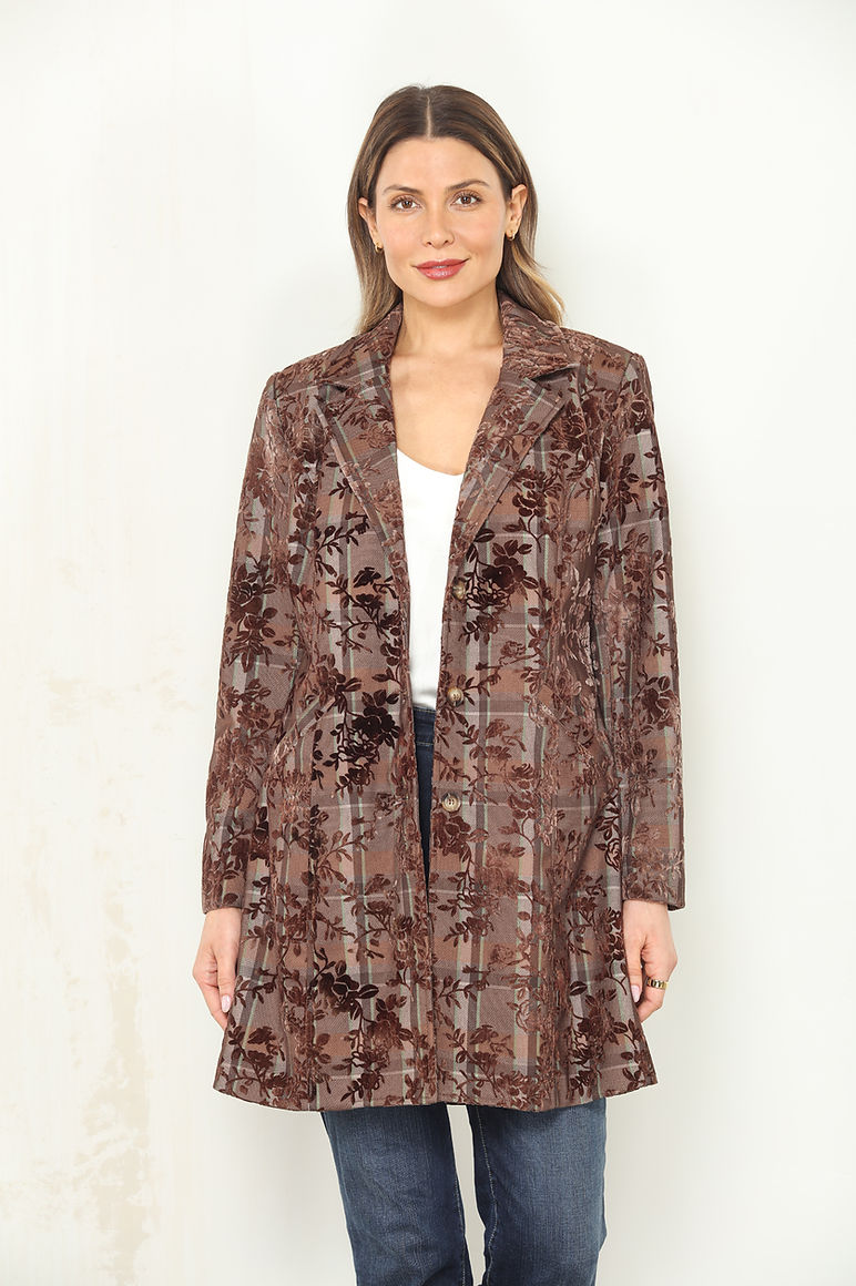 A woman modeling an espresso brown and beige flocked plaid floral patterned open-front mid-length jacket over a white top and blue jeans, standing against a light off-white wall.