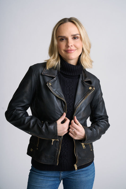 Woman wearing a black leather hazie jacket over a dark sweater with a plain background