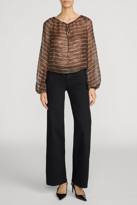 Woman wearing a brown and metallic long sleeve sheer shirt with Frame Black Low rise Le Slim Palazzo pants and black heels on a plain background.