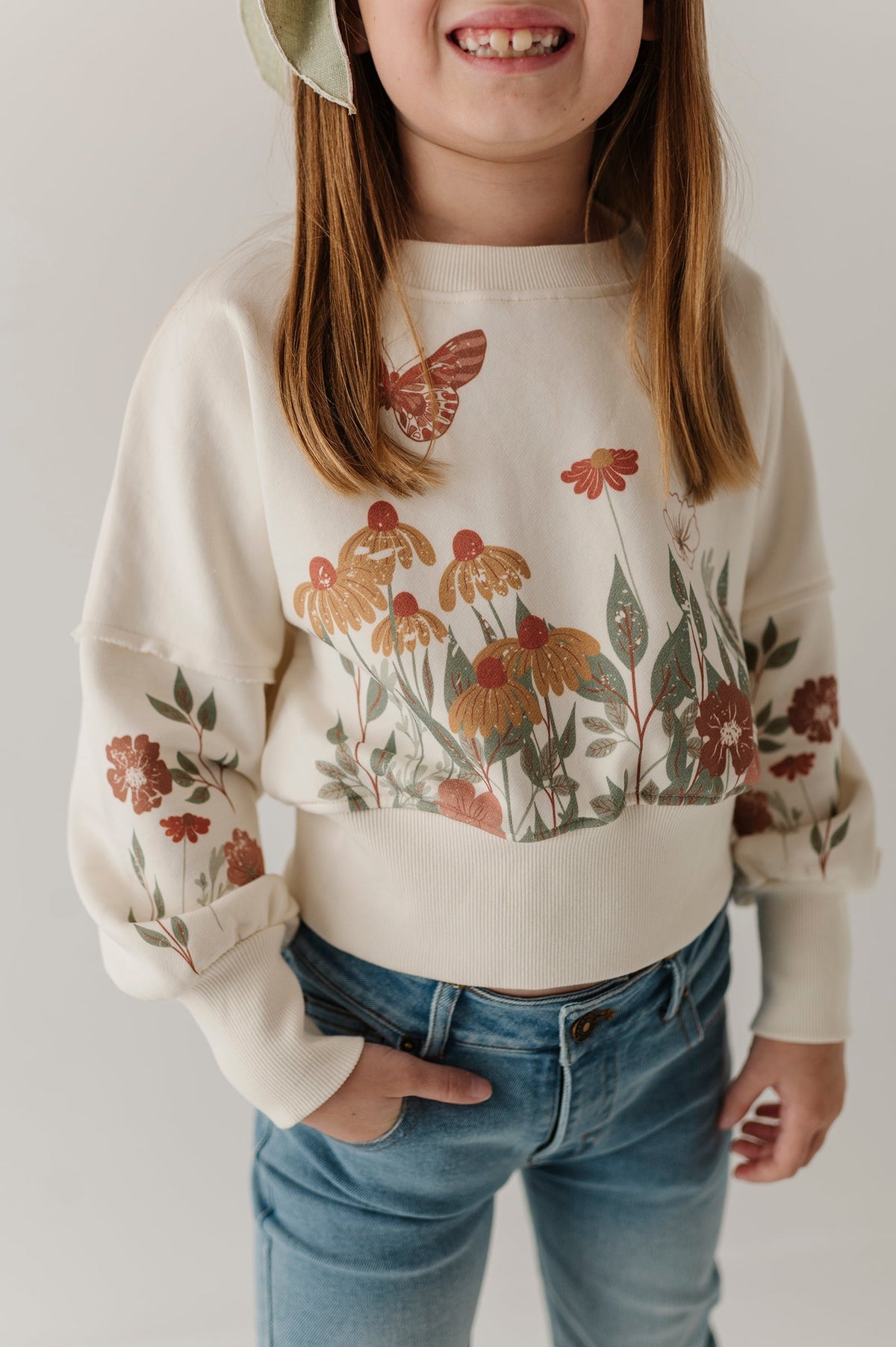Child wearing a cream sweater with floral garden design and blue jeans on a plain background