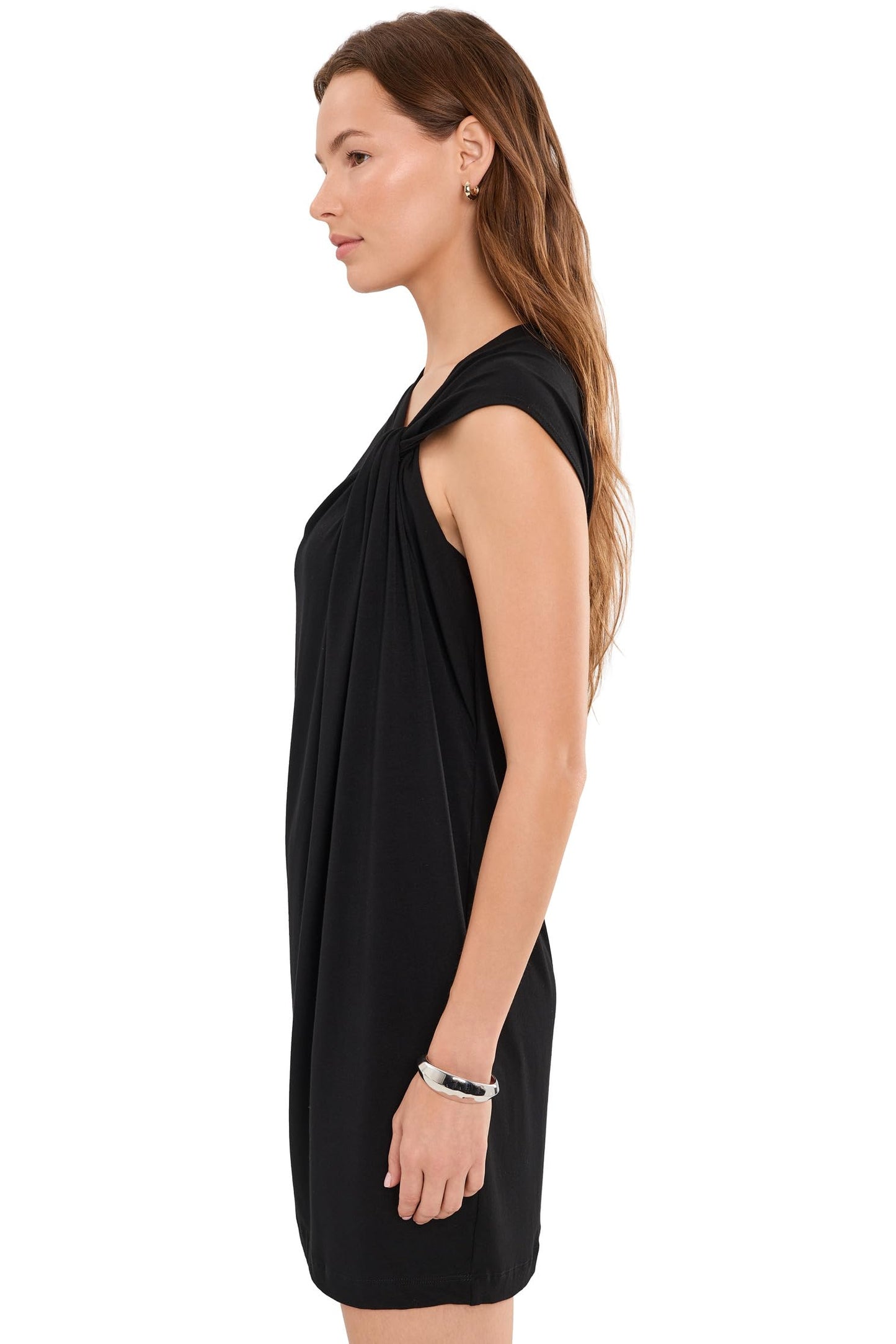 A woman shown in side profile wearing a sleeveless twist shoulder black draped minidress against a plain white background.