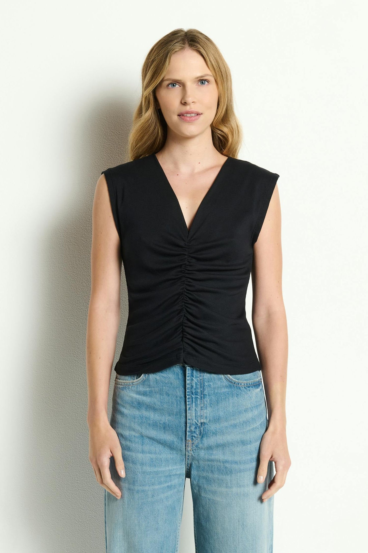 Woman wearing a black sleeveless Lune shirred front tank top and blue jeans against a white background