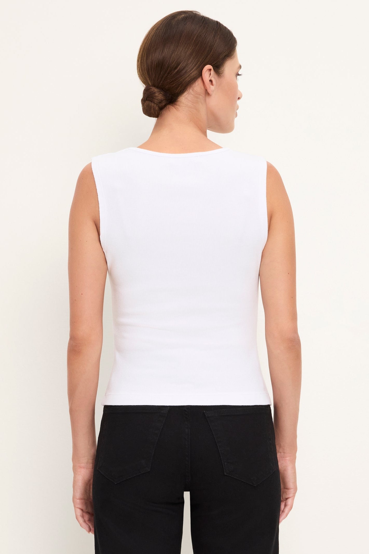A woman shown from the back wearing a fitted sleeveless white top and black pants against a plain light background.