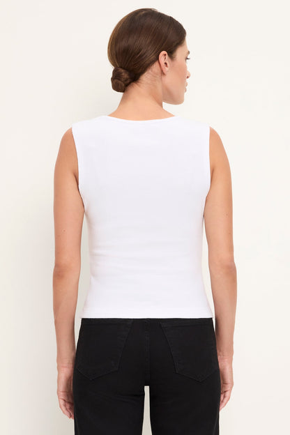 A woman shown from the back wearing a fitted sleeveless white top and black pants against a plain light background.