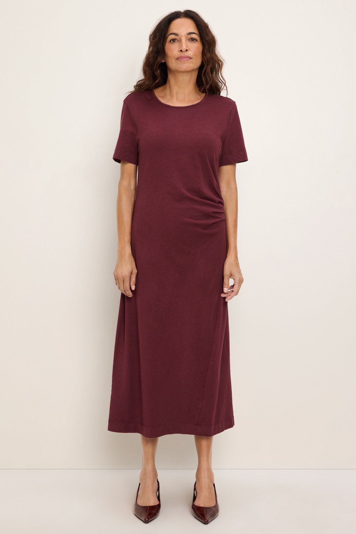 A woman modeling a short-sleeve, crew-neck emeline column midi dress in port royale color, standing against a plain off-white studio background.