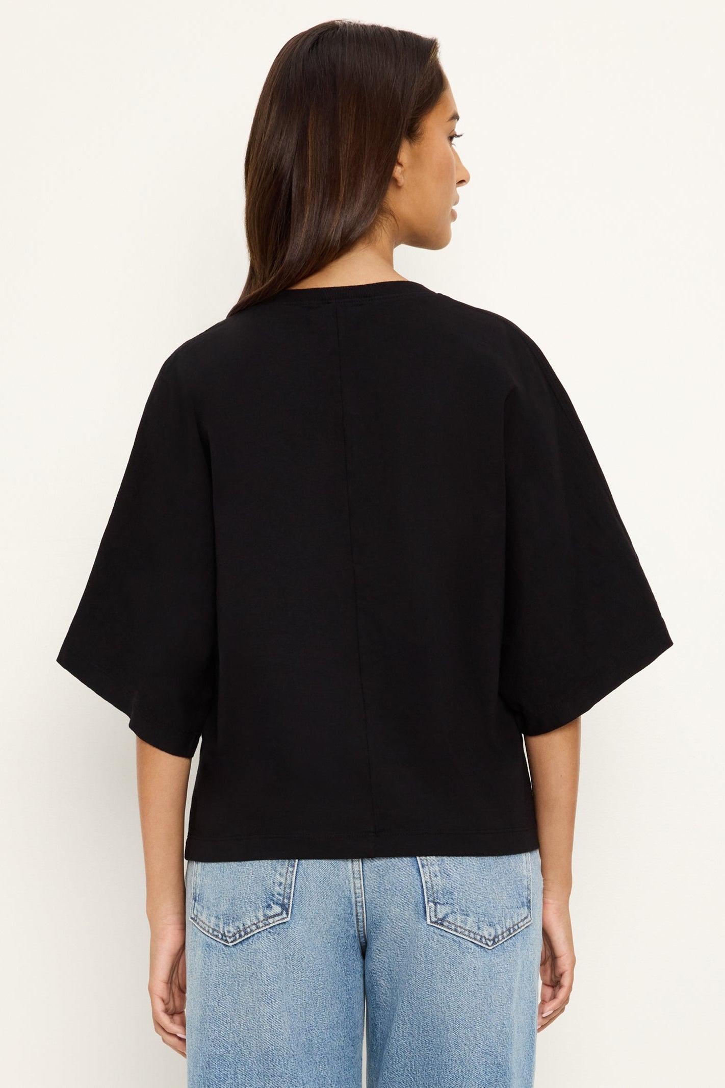 Person wearing a black oversized cape sleeve shirt and light blue jeans on a white background