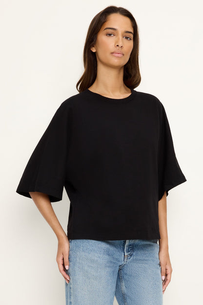 Person wearing a black oversized cape sleeve tee and blue jeans on a white background