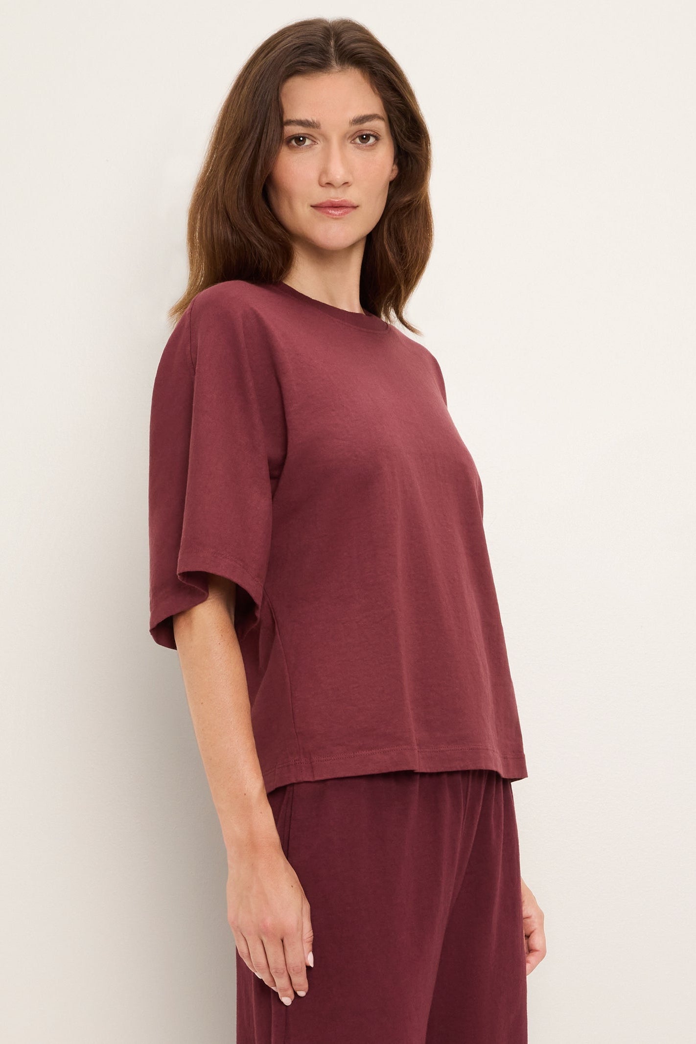 A woman modeling a loose-fitting short-sleeve top and matching pants in a port royale burgundy color, photographed against a plain off-white studio background.