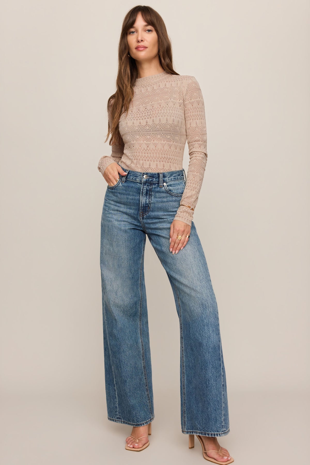 Woman wearing a soft ecru beige avery sweater and blue jeans on a plain background