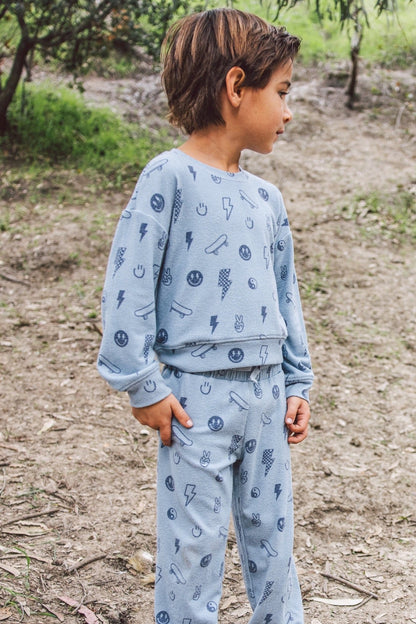 A child wearing a light celestial blue pajama set with a dark blue pattern of small icons, standing outdoors on a dirt path.