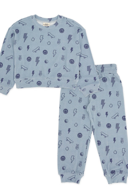 A two-piece kids' loungewear set in light  celestial blue, featuring a long-sleeve top and matching jogger pants with an allover dark blue graphic print of lightning bolts, smiley faces, and peace signs, shown on a plain white background.