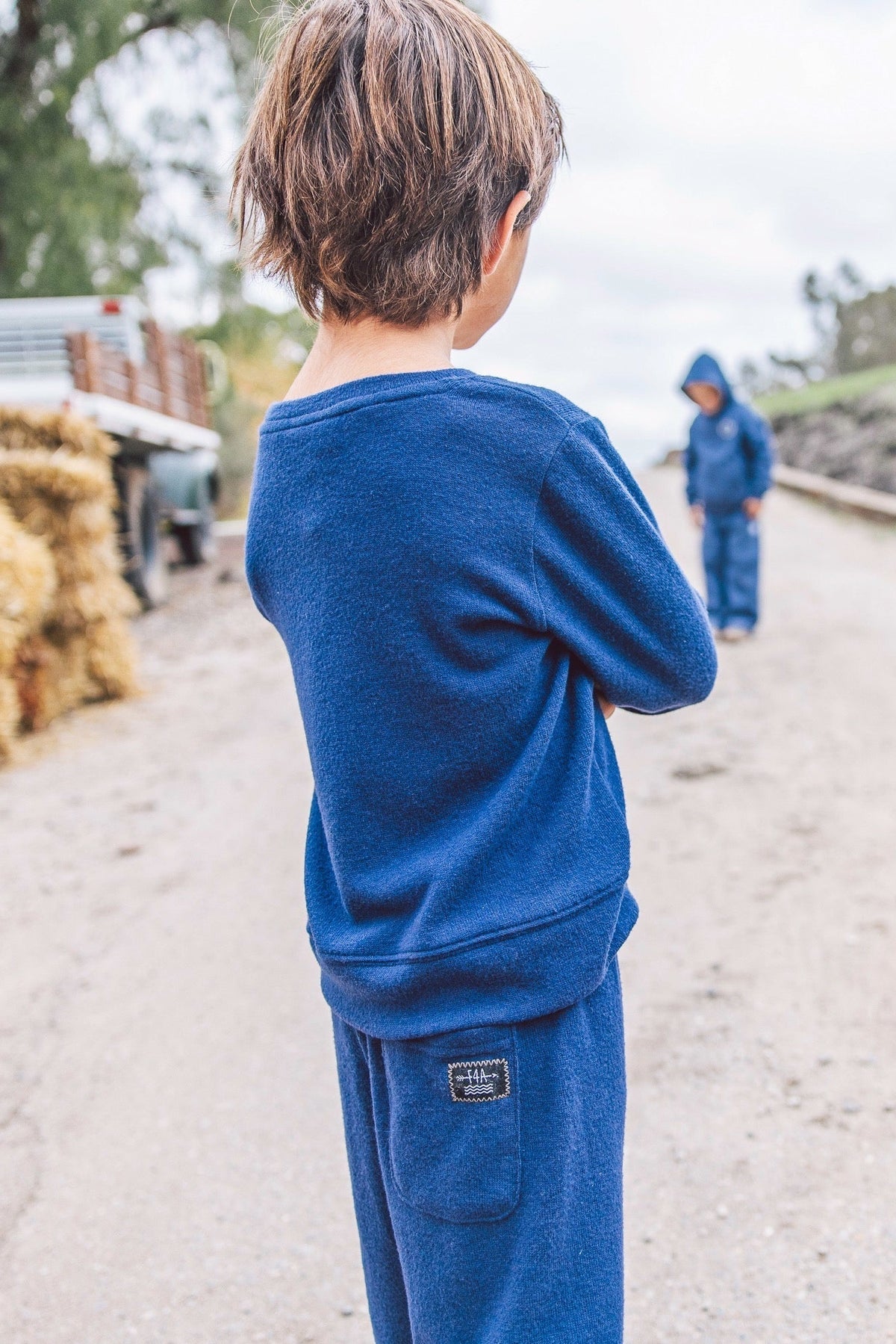 A child wearing a matching crown blue sweatshirt and sweatpants set, viewed from behind on an outdoor dirt path.