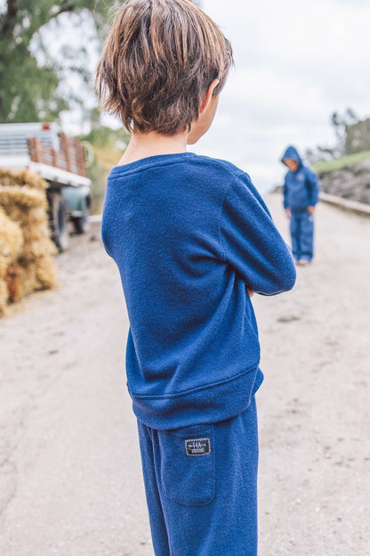 A child wearing a matching crown blue sweatshirt and sweatpants set, viewed from behind on an outdoor dirt path.