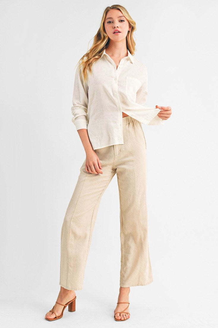 A woman modeling a light cream linen button-down shirt and khaki wide-leg linen trousers against a plain white studio background.