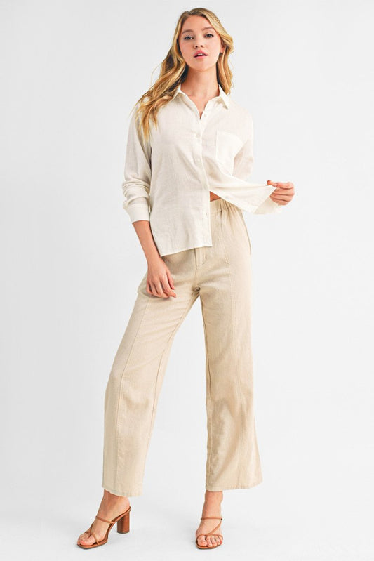 A woman modeling a light cream linen button-down shirt and khaki wide-leg linen trousers against a plain white studio background.