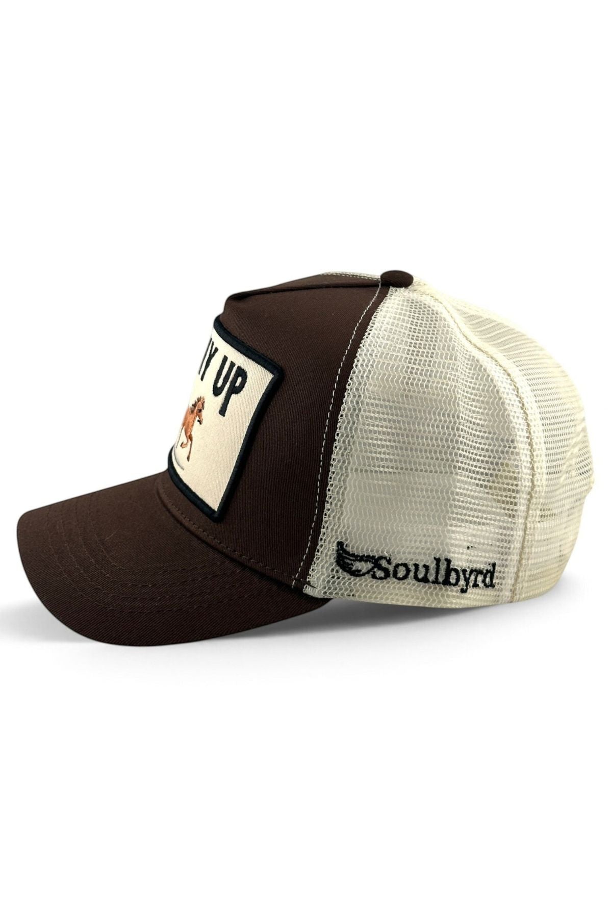 A brown and cream trucker hat with a dark brown front panel and brim, cream mesh back panels, a patch on the front with a horse graphic and partial text, and the brand name 'Soulbyrd' embroidered on the side.