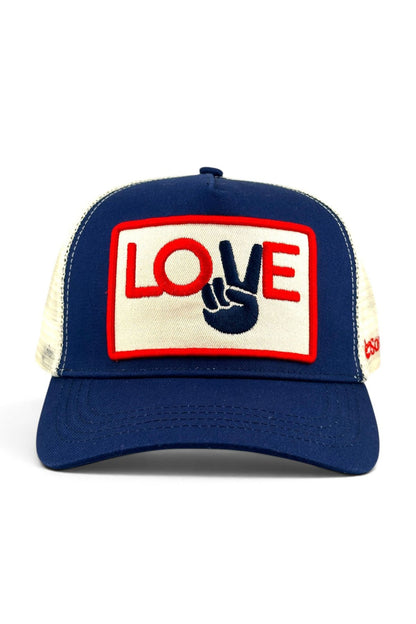A navy blue trucker hat with cream mesh side panels and a front patch reading 'LOVE' in red and navy, with a navy peace symbol inside the word 'LOVE'.