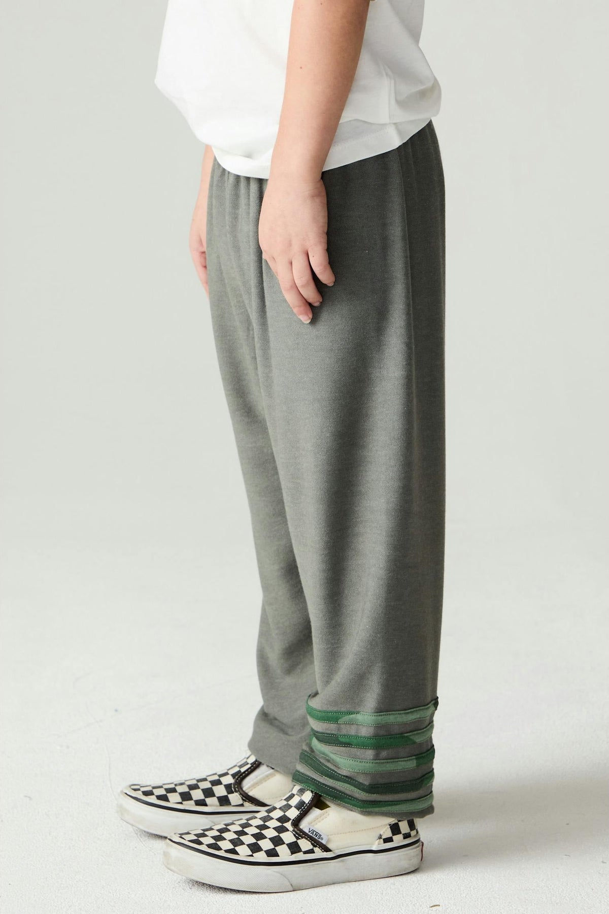 Boy shown from the side wearing safari green jogger style pants with green camo stripe accents and black and white checkered Vans tennis shoes on a plain background