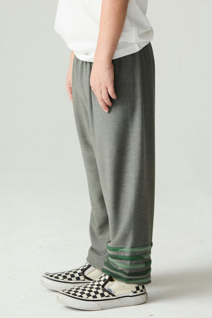 Boy shown from the side wearing safari green jogger style pants with green camo stripe accents and black and white checkered Vans tennis shoes on a plain background