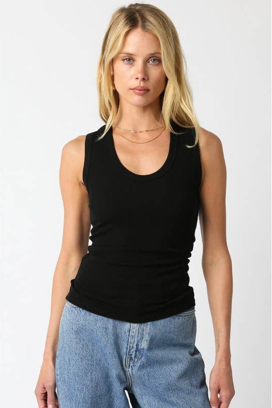 Woman wearing a black tank top with light blue jeans on a plain background 