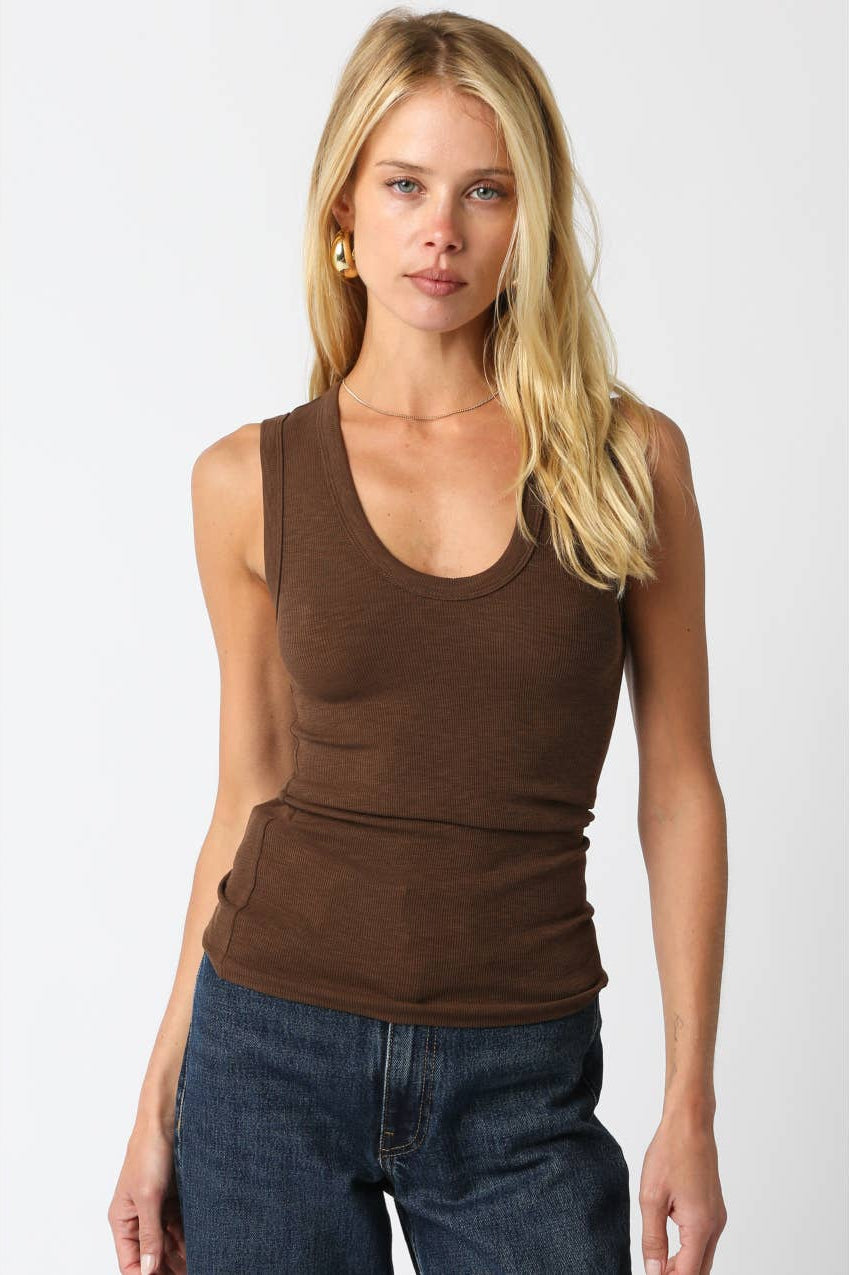 Woman wearing a thick strap brown tank top with dark blue jeans on a plain background 
