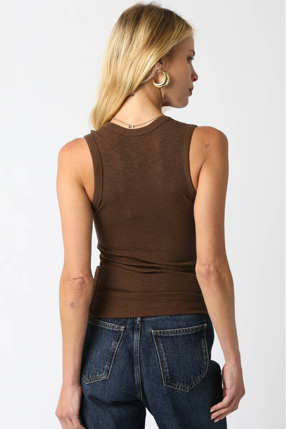 Woman shown from the back wearing a brown tank top and dark blue jeans on a plain background