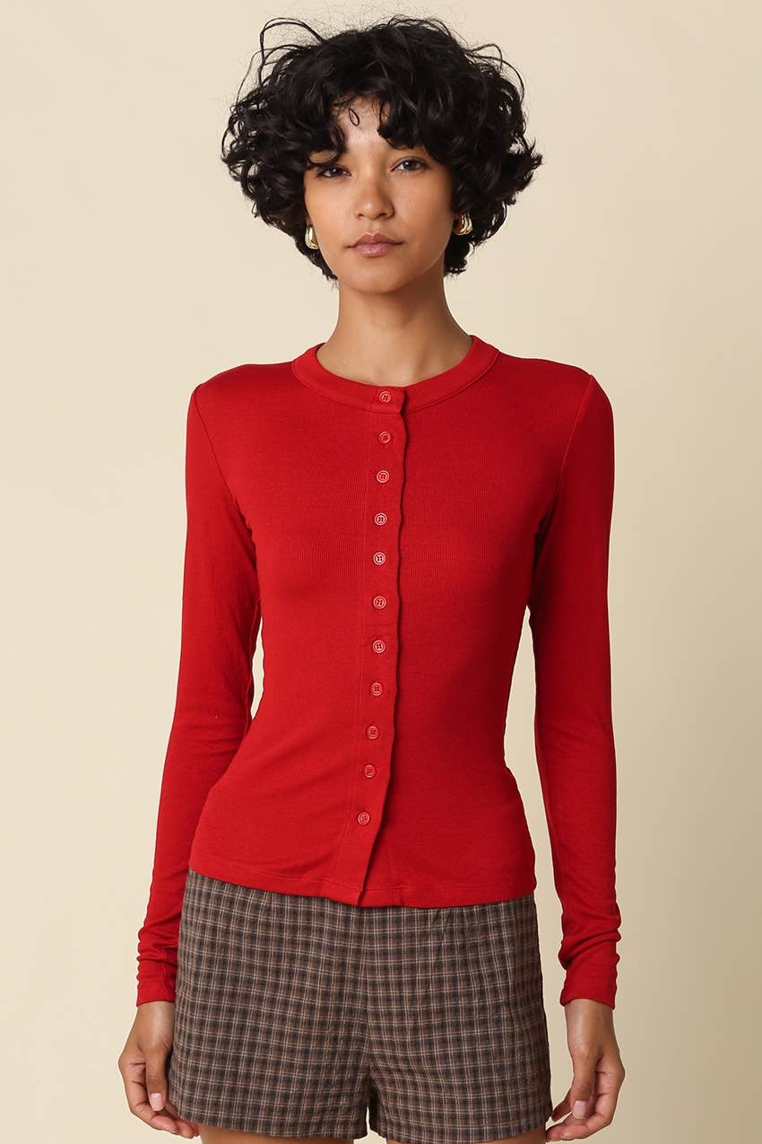 Woman wearing a ruby red long-sleeve shirt and plaid shorts on a beige background