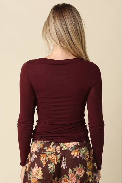 Woman shown from the back wearing a burgundy long sleeve top with burgundy floral pants and pink flats on a plain background 