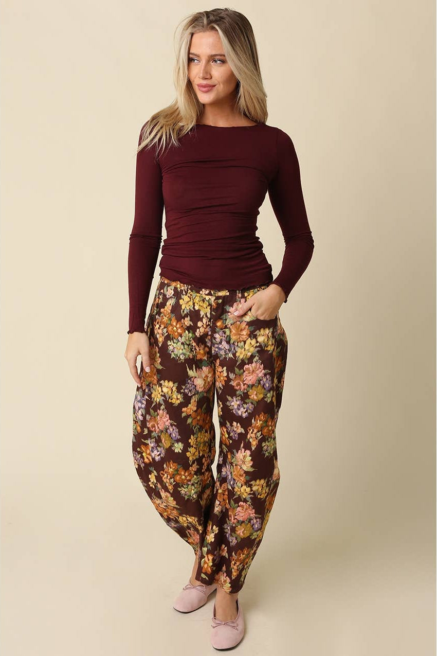 Woman wearing a burgundy long sleeve top with burgundy floral pants and pink flats on a plain background 