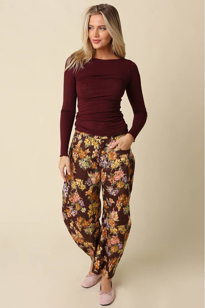 Woman wearing a burgundy long sleeve top with burgundy floral pants and pink flats on a plain background 