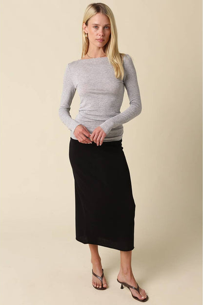 Woman shown from the front wearing a heather grey long sleeve shirt and black midi skirt with heels 